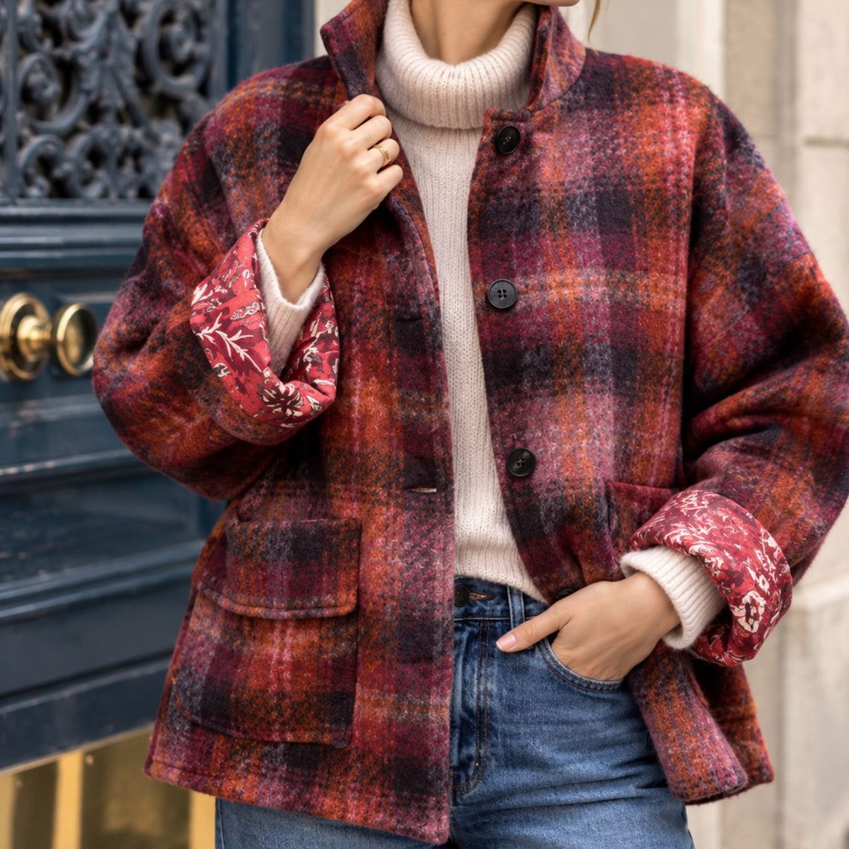 Veste Johanna à carreaux bordeaux et orangés, portée avec un pull écru et un jean, doublure imprimée visible aux poignets.