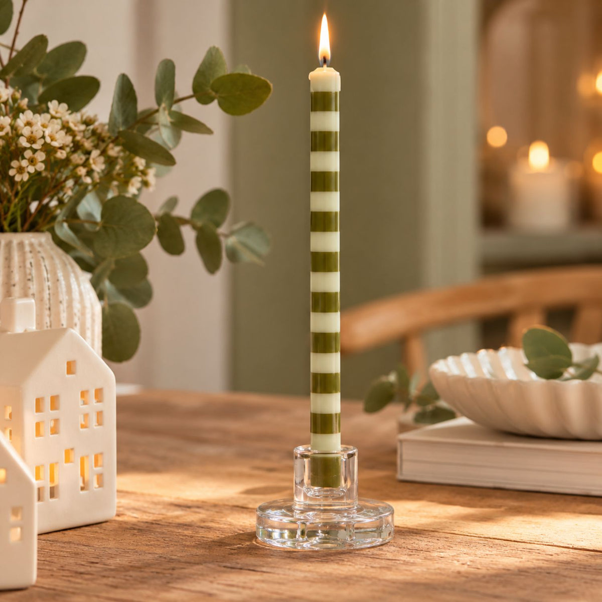 Bougie fine rayée vert olive et écru Ib Laursen dans un bougeoir en verre transparent, sur une table en bois à la décoration chaleureuse.